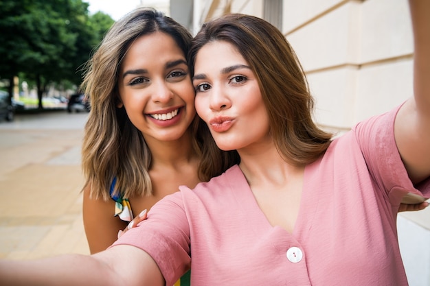 Due giovani amici sorridenti e prendendo un selfie stando in piedi all'aperto. Concetto urbano.