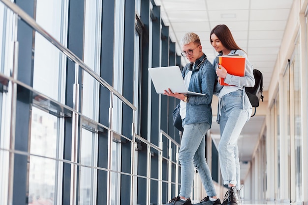 Due giovani amici studenti insieme in un corridoio di un college con il laptop in mano