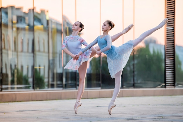 Due giovani ballerine in scarpe da punta stanno ballando sullo sfondo del riflesso del tramonto della città nella parete specchiata dell'edificio