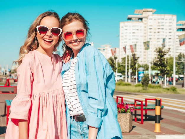 Due giovani belle donne hipster sorridenti in abiti estivi alla moda Donne spensierate sexy in posa per strada Modelli puri positivi che si divertono al tramonto abbracciandosi e impazzendo Felici e allegri