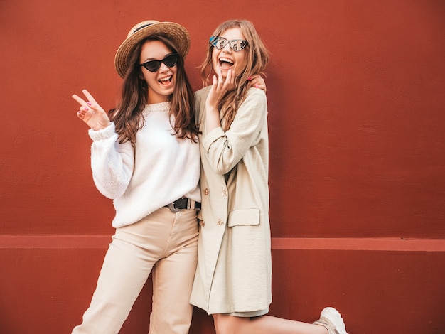 Due giovani belle donne hipster sorridenti in maglione e cappotto bianchi alla moda