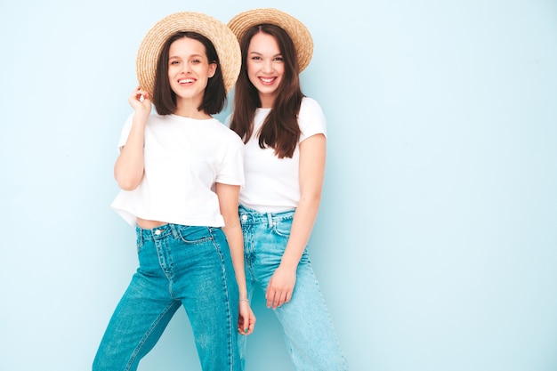 Due giovani belle donne hipster sorridenti in t-shirt bianca estiva alla moda e vestiti di jeans