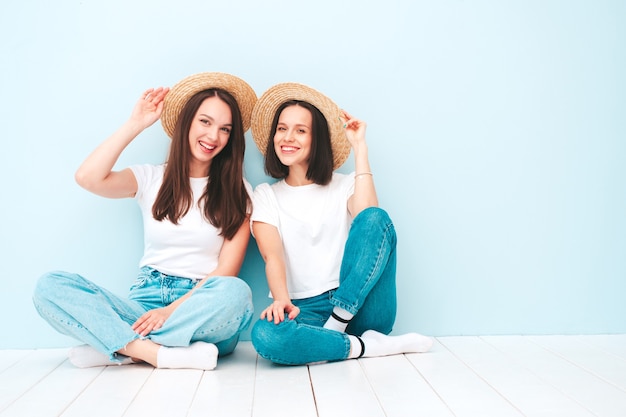 Due giovani belle donne hipster sorridenti in t-shirt bianca estiva alla moda e vestiti di jeans