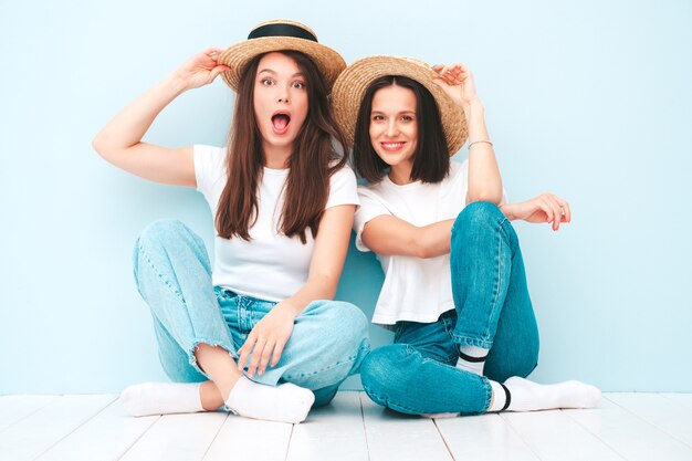 Due giovani belle donne hipster sorridenti in t-shirt bianca estiva alla moda e vestiti di jeans