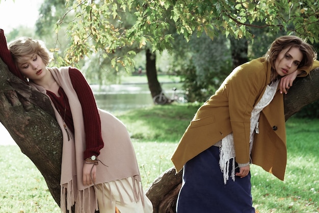 Due giovani belle donne in posa su un albero, parco autunnale