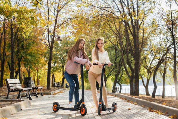 Due giovani belle ragazze guidano scooter elettrici nel parco in una calda giornata autunnale