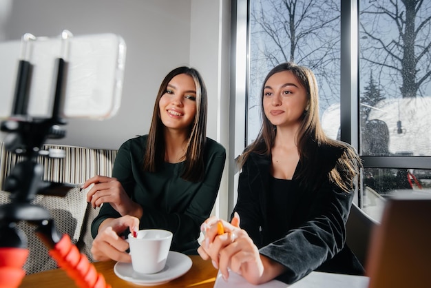 Due giovani belle ragazze sono sedute in un bar, registrano video blog e comunicano sui social network.