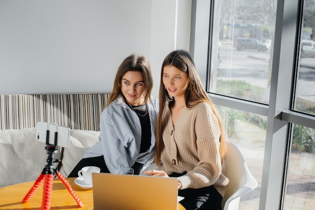 Due giovani belle ragazze sono sedute in un bar, registrano video blog e comunicano sui social network.