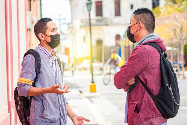 Due giovani con maschera che conversano all'aperto due amici con maschera facciale che hanno un concetto di conversazione di conversazione e distanza sociale