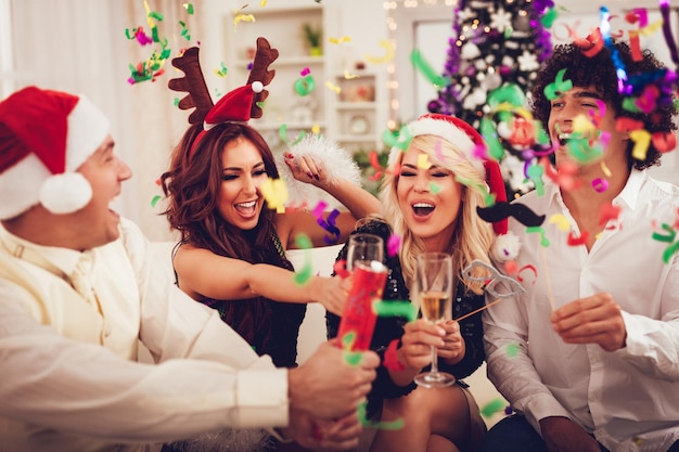 Due giovani coppie allegre che celebrano il Natale con i coriandoli a casa. Si divertono e brindano con lo champagne.