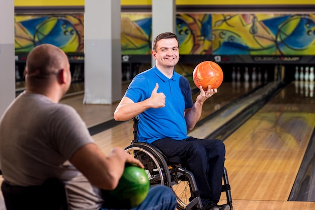 Due giovani disabili in sedia a rotelle che giocano a bowling nel club