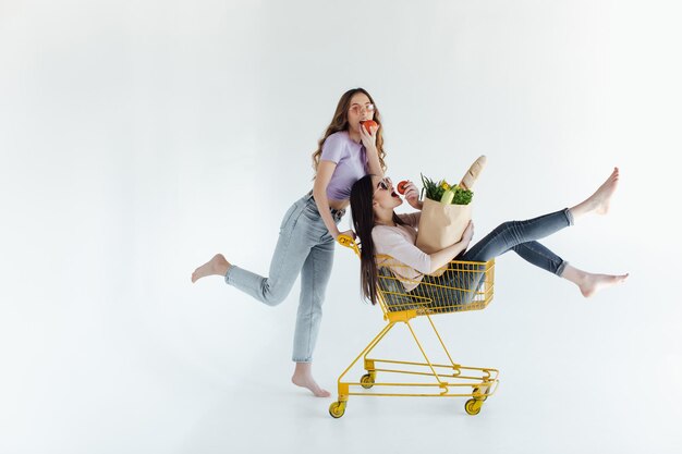 Due giovani donne allegre in abiti colorati alla moda che sorridono e si divertono con il carrello