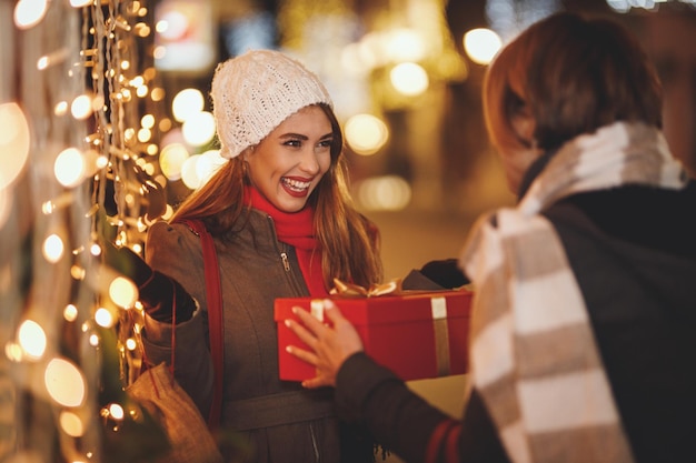 Due giovani donne allegre si divertono nella strada della città la notte di Natale. Stanno ridendo e si scambiano regali per le vacanze.