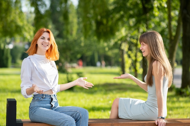 Due giovani donne amici seduti su una panchina nel parco estivo e parlando con una discussione.