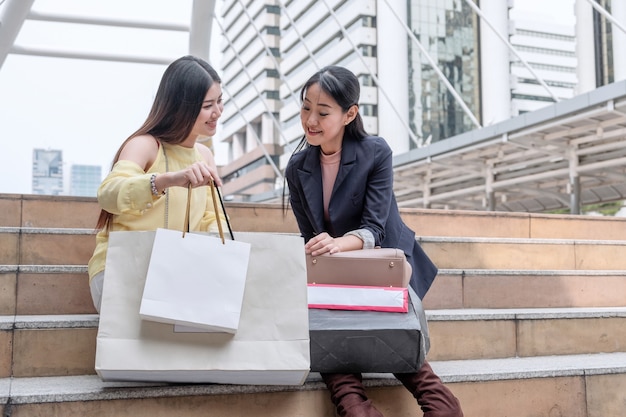 Due giovani donne asiatiche che tengono le borse della spesa e guardano le scale in città