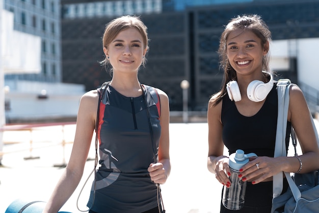 Due giovani donne atletiche sorridenti felici che camminano insieme all'aperto dopo l'allenamento sportivo, parlando e abbracciandosi.