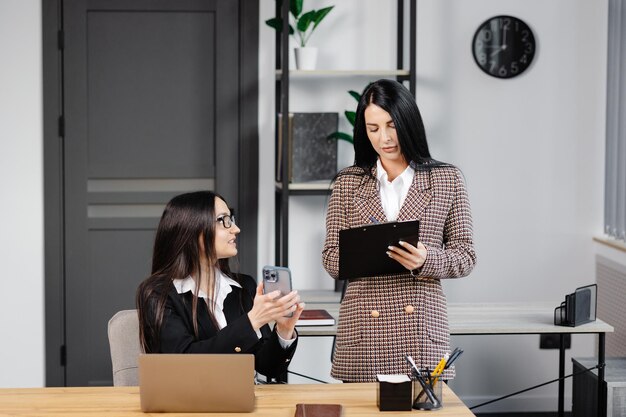 Due giovani donne attraenti stanno lavorando in ufficio una donna sta parlando al telefono e il suo collega sta facendo appunti in un quaderno