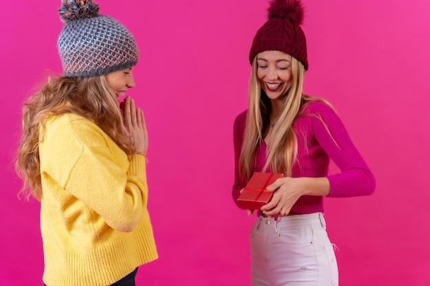 Due giovani donne caucasiche bionde che danno un regalo per un compleanno su un isolato su uno sfondo rosa