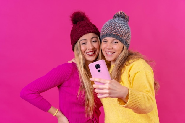 Due giovani donne caucasiche bionde con un telefono isolato su uno sfondo rosa selfie sorridente