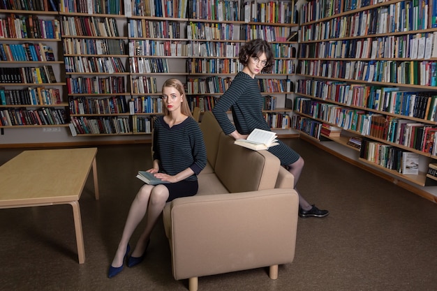 Due giovani donne caucasiche seduti in biblioteca con i libri