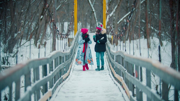 Due giovani donne che bevono bevande calde dal thermos e camminano sul ponte innevato