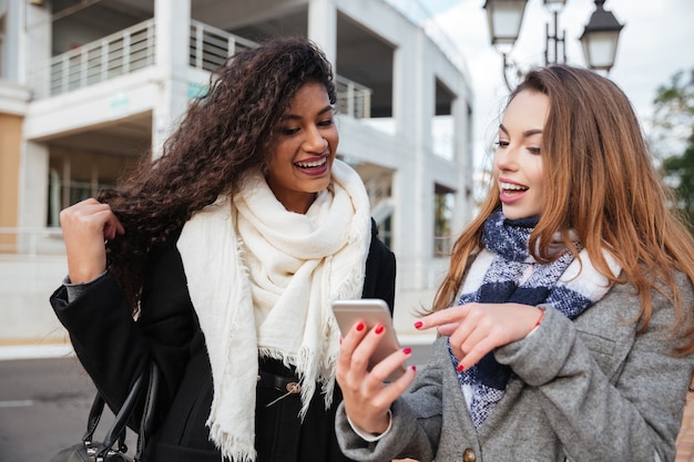 due giovani donne che guardano su uno smartphone e puntano allo schermo sorpresi.