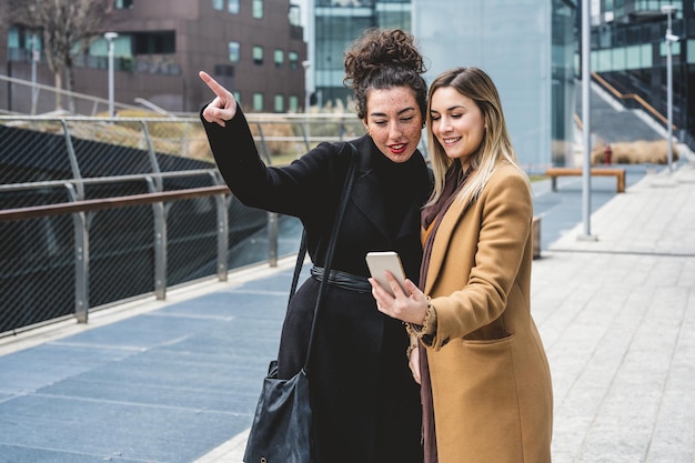 Due giovani donne che viaggiano per la città utilizzando lo smartphone per cercare informazioni e mappe che indicano un luogo che stanno cercando