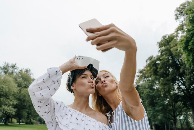 Due giovani donne con occhiali VR si fanno un selfie in un parco