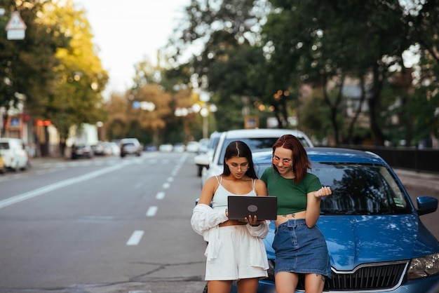 Due giovani donne con un computer portatile vicino all'auto