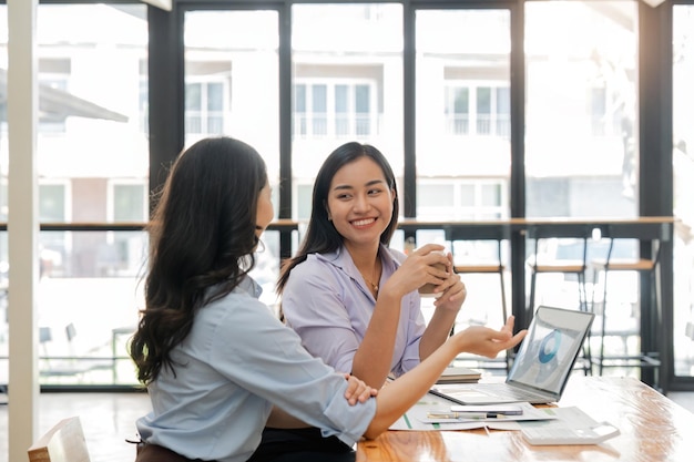 Due giovani donne d'affari asiatiche discutono della strategia di lavoro e pianificazione del progetto di investimento Uomini d'affari che parlano insieme al computer portatile in ufficio