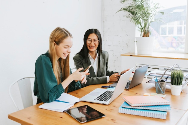 Due giovani donne d'affari professioniste in abiti da cerimonia lavorano in un ufficio moderno utilizzando un tablet portatile e cercano soluzioni insieme, una ragazza asiatica indipendente e sicura di sé risolve i problemi