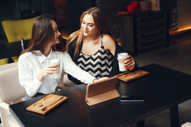 Due giovani donne di affari alla moda che si siedono in un caffè e usano il ridurre in pani