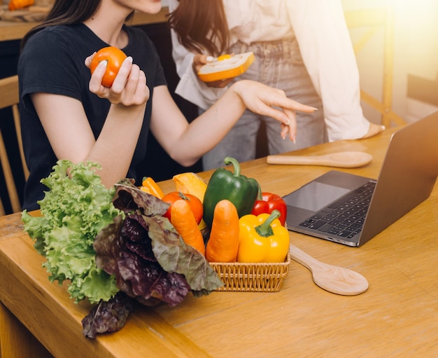 Due giovani donne felici che guardano il computer portatile durante la cottura insieme nella stanza della cucina a casa Due giovani donne lesbiche diverse trascorrono del tempo insieme LGBT e concetto di identità di genere