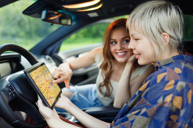 Due giovani donne felici guidano viaggiatori turisti con tablet digitali Stati Uniti mappa americana in veicolo a noleggio