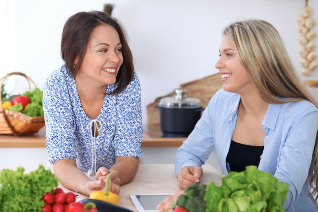 Due giovani donne felici stanno facendo acquisti online tramite computer tablet e carta di credito Gli amici cucineranno in cucina