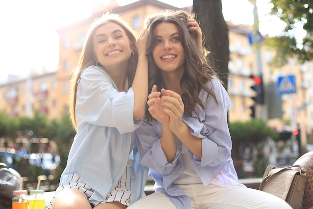 Due giovani donne hipster sorridenti in abiti estivi in posa sulla strada. Femmina che mostra emozioni positive per il viso.