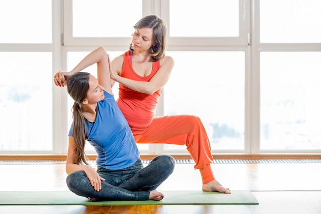 Due giovani donne in abiti sportivi colorati che fanno esercizi di stretching seduti su un tappetino yoga massaggio tailandese