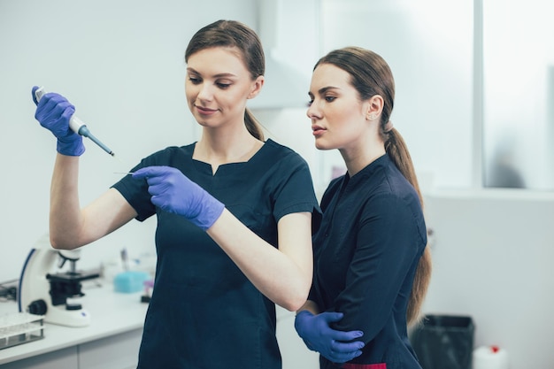 Due giovani donne in uniforme medica in piedi nel laboratorio e lavorano con i campioni