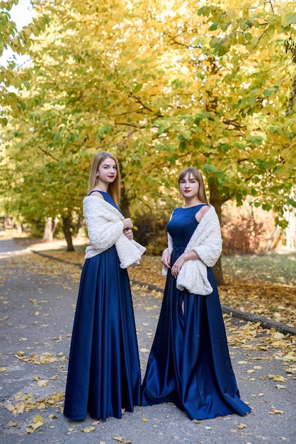 Due giovani donne molto belle in abiti blu alla moda nel parco autunnale.