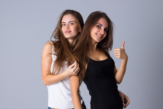 Due giovani donne positive in camicie bianche e nere che si abbracciano su sfondo grigio in studio