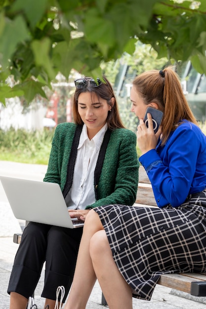 Due giovani donne sedute su una panchina di strada che lavorano sul loro laptop che punta allo schermo