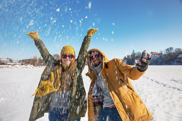 Due giovani felici che lanciano neve e si divertono Giornata di sole invernale di messa a fuoco selettiva