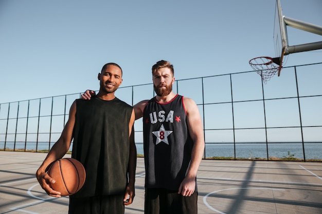 Due giovani giocatori di basket in piedi insieme al parco giochi e guardando davanti