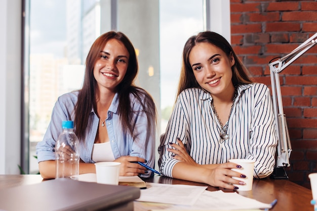 Due giovani imprenditrici che si siedono allo scrittorio del lavoro nel corso della riunione d'affari nella moderna sala per conferenze