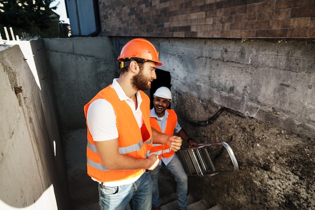 Due giovani ingegneri maschi in uniforme e elmetto protettivo che lavorano in cantiere