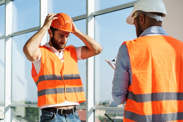 Due giovani ingegneri maschi in uniforme e elmetto protettivo che lavorano in cantiere