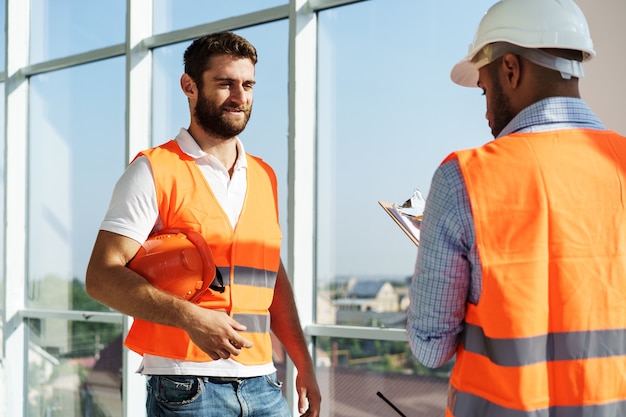 Due giovani ingegneri maschi in uniforme e elmetto protettivo che lavorano in cantiere