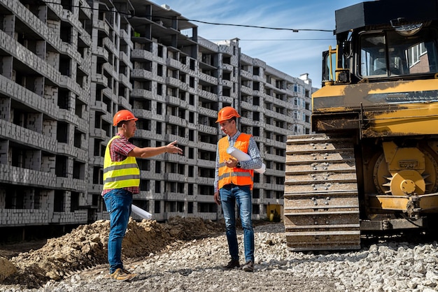 Due giovani operai in divisa stanno valutando un progetto per costruire una nuova casa