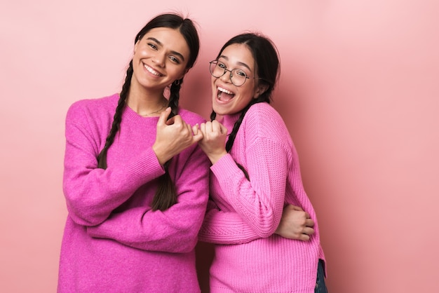 due giovani ragazze adolescenti con le trecce si agganciano a vicenda le piccole dita in conciliazione o amicizia isolate su un muro rosa