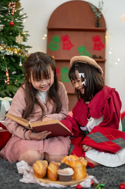 Due giovani ragazze asiatiche felici si divertono a leggere una favola di Natale in un libro